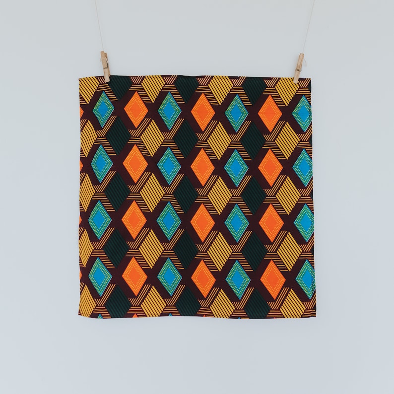 May include: A brown fabric with a geometric pattern of orange, yellow, blue, and green diamonds. The fabric is hanging from two clothespins.