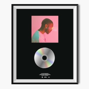 May include: A framed black and white photo of a man with a CD in the center. The photo is of a man with short dark hair, wearing a white shirt and looking down. The photo is framed in a black frame with a white mat. The CD is silver with a rainbow effect. The text "FOREVER" is visible in the photo.
