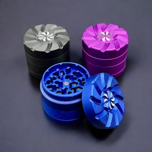 May include: Three metal grinders with different colored tops: gray, purple, and blue. The grinders have a unique design with a swirl pattern on the top.