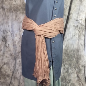 May include: A sleeveless dark gray tunic featuring a front button placket with silver-toned buttons, paired with light green trousers. A textured brown sash is tied around the waist, featuring long ends with small dark brown tassels at the bottom.