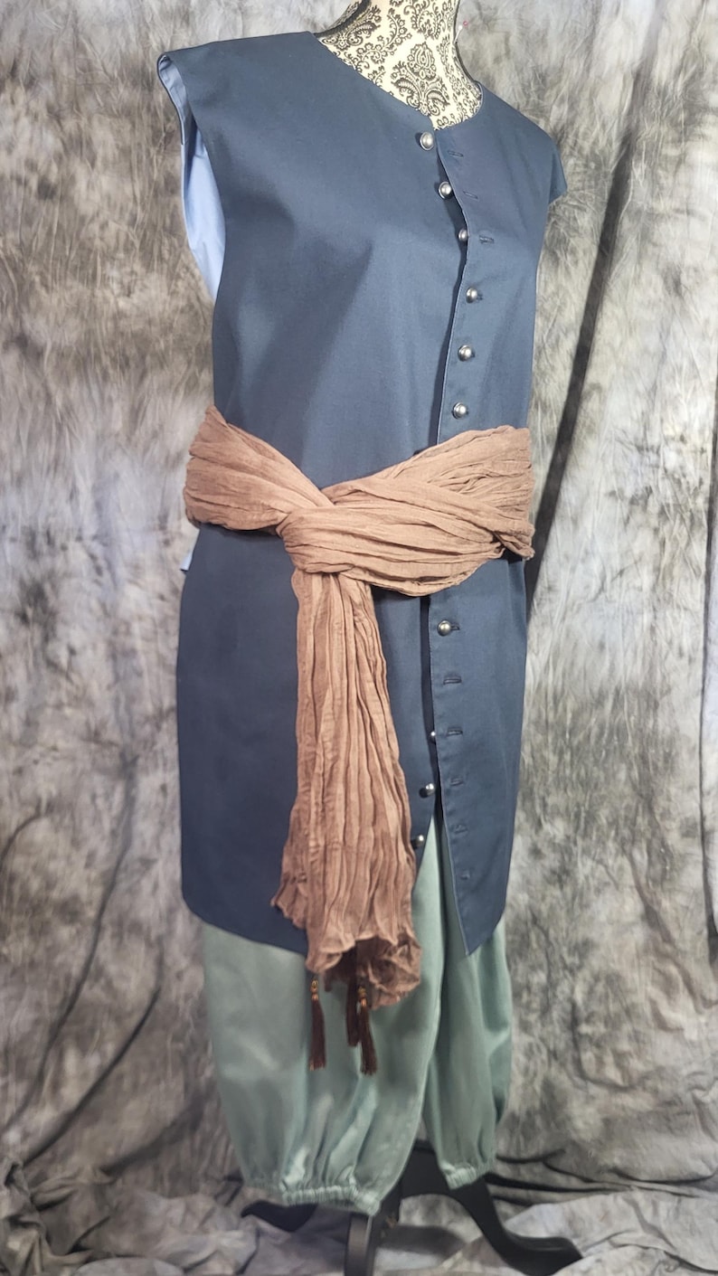 May include: A sleeveless dark gray tunic featuring a front button placket with silver-toned buttons, paired with light green trousers. A textured brown sash is tied around the waist, featuring long ends with small dark brown tassels at the bottom.