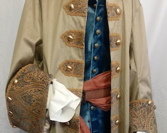 May include: A tan pirate costume with gold accents, including a long coat, a blue velvet vest, and a brown sash. The coat features decorative gold buttons and paisley patterned cuffs. A white collared shirt is visible underneath.