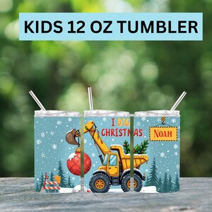 May include: A 12 oz tumbler for kids with a winter theme. The tumbler features a yellow construction vehicle lifting a Christmas ornament. The text "I DIG CHRISTMAS" and a name are also displayed on the tumbler.