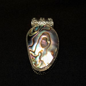 Puede incluir: Un colgante de plata con una gran incrustación de nácar de abulón iridiscente. La concha tiene un patrón de remolinos de azules, verdes y morados.