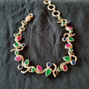 Peut inclure: Un bracelet en argent avec un motif de vigne orné de pierres précieuses vertes, roses et bleues.
