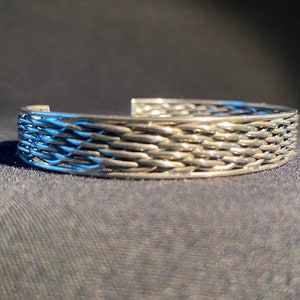 May include: A silver bracelet with a woven design. The bracelet is made of a series of interlocked metal strands.