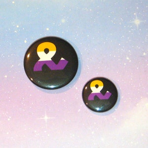 May include: Two round black button badges with a white ampersand symbol on a purple, yellow, and white background. The larger badge is 2.5 cm in diameter and the smaller badge is 2 cm in diameter.
