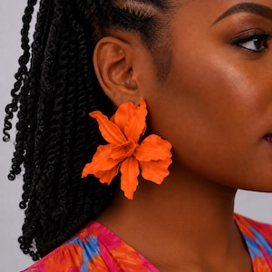 May include: A large, vibrant orange earring shaped like a blooming flower with layered, wavy petals. The earring features a matte finish and a structured design that mimics the organic curves of a floral blossom, creating a bold statement piece.