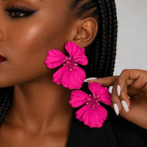 May include: A pair of vibrant hot pink flower-shaped earrings featuring layered, wavy petals and a central cluster of matching pink beads. The earrings have a matte finish and a bold, oversized design that creates a striking visual statement.