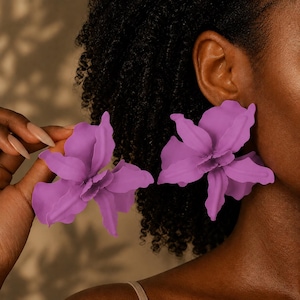 May include: A pair of large, matte purple flower-shaped earrings with layered, wavy petals. The earrings feature a bold, oversized design that mimics the appearance of a blooming orchid, with a smooth, solid-colored finish throughout the structure.