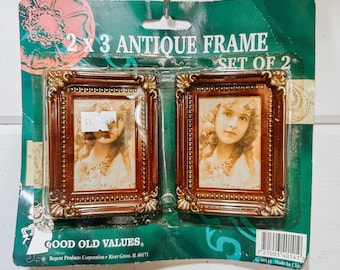 May include: Two antique picture frames, each 2x3 inches, displayed on a green and white card. The frames are brown with gold accents and contain sepia-toned portraits of a young girl. The packaging reads "2 x 3 Antique Frame, Set of 2."