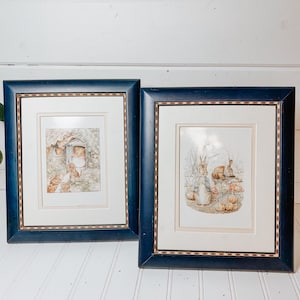 Pode incluir: Duas gravuras emolduradas com ilustrações de coelhos de Beatrix Potter. Cada gravura está numa moldura de madeira azul-escura com uma borda interior decorativa, passe-partout branco e vidro, exibindo cenas detalhadas de coelhos na natureza.