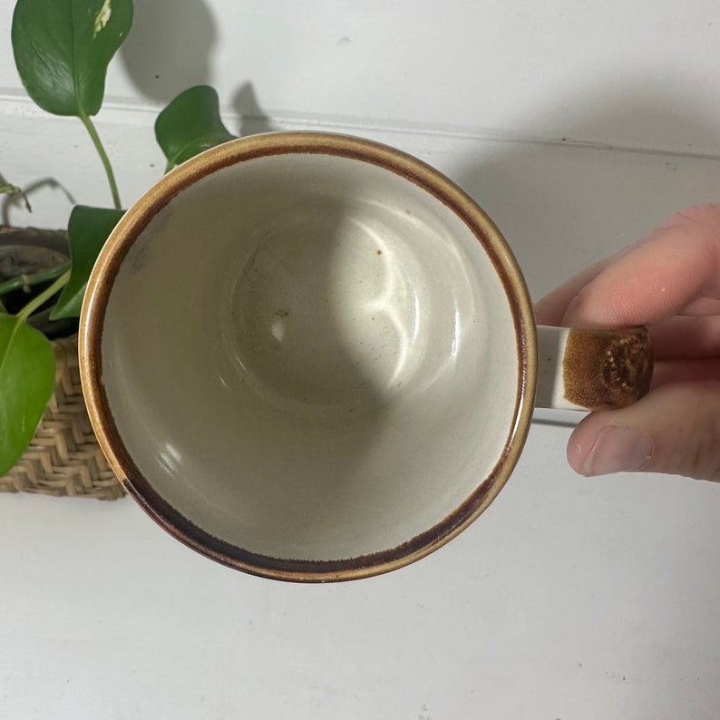 Puede incluir: Una taza de cer&aacute;mica marr&oacute;n y blanca con un borde y un asa marrones. La taza est&aacute; vac&iacute;a y el interior es blanco.