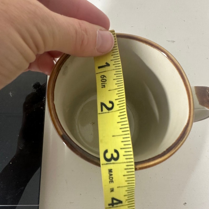 Puede incluir: Una taza de cer&aacute;mica marr&oacute;n y blanca con un borde marr&oacute;n, medida con una cinta m&eacute;trica amarilla. La cinta m&eacute;trica indica 3 pulgadas.
