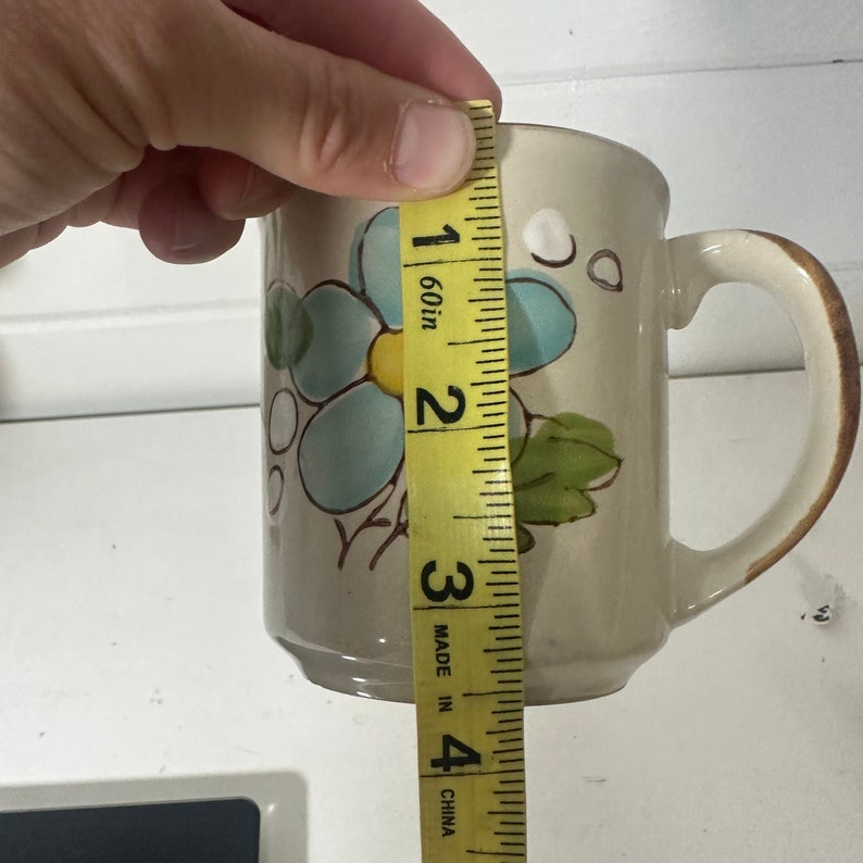 Puede incluir: Una taza de cer&aacute;mica beige con un dise&ntilde;o floral azul y amarillo. La taza mide 9 cm de alto. "Made in China" est&aacute; impreso en la cinta m&eacute;trica.