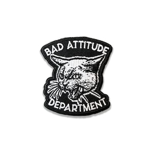May include: Black and white embroidered patch with a cat's face and the text "Bad Attitude Department".
