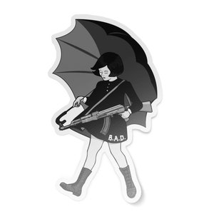 May include: Black and white illustration of a girl holding a rifle and walking under an umbrella. The girl is wearing a black dress and boots. The text "B.A.D." is printed on the dress.