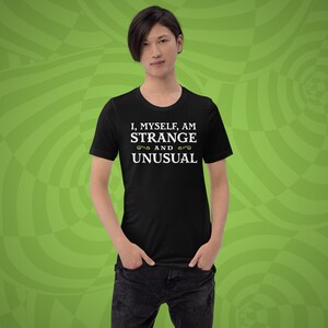 May include: A black t-shirt with white text that reads "I, myself, am strange and unusual".