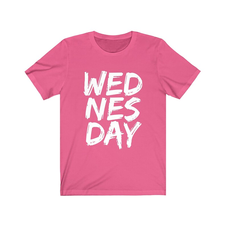 Puede incluir: Camiseta rosa de manga corta con el texto "WEDNES DAY" en blanco, con letras estilizadas.