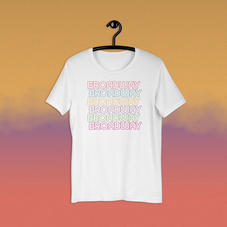 May include: White t-shirt with the word "BROADWAY" repeated six times in a rainbow of colours. Each word is outlined in a slightly darker shade of the same colour.