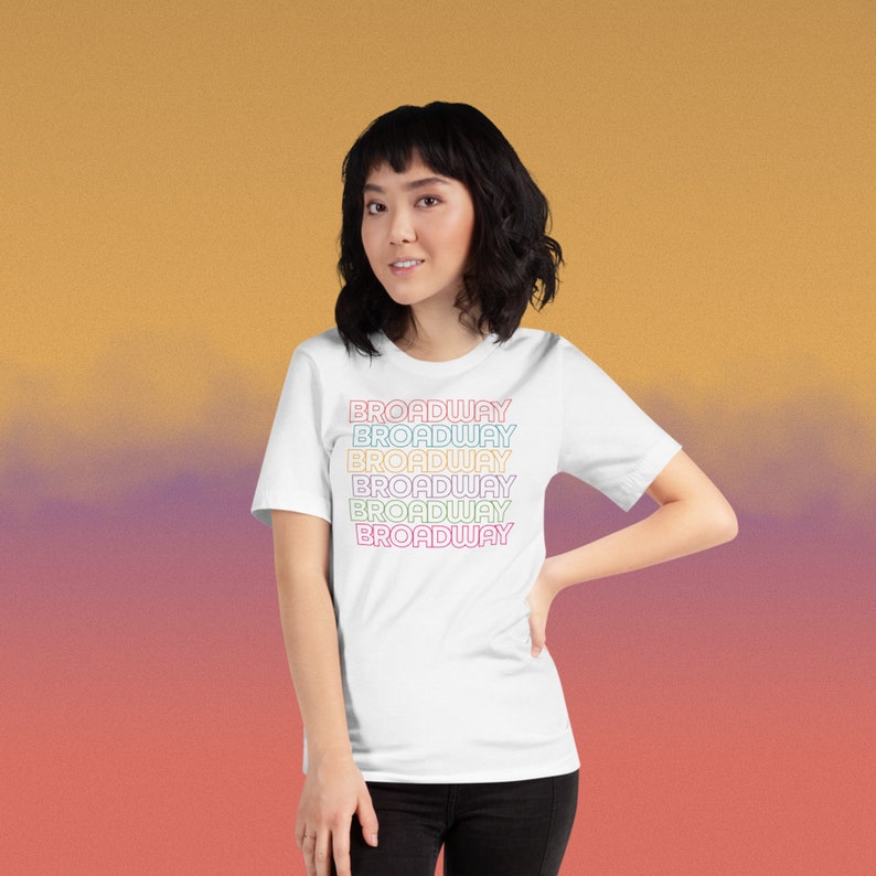 May include: White t-shirt with the word "BROADWAY" repeated five times in a rainbow gradient.