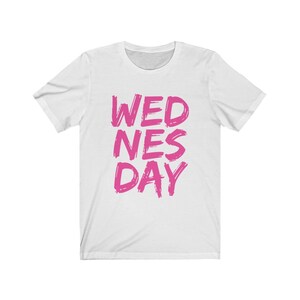 Puede incluir: Camiseta blanca con el texto "WEDNES DAY" en letras rosas.