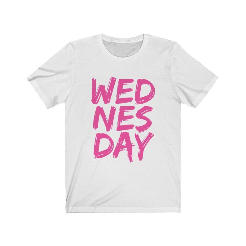 Puede incluir: Camiseta blanca con el texto "WEDNES DAY" en letras rosas.