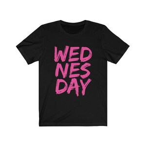 Puede incluir: Camiseta negra con las palabras "WEDNES DAY" escritas en rosa.