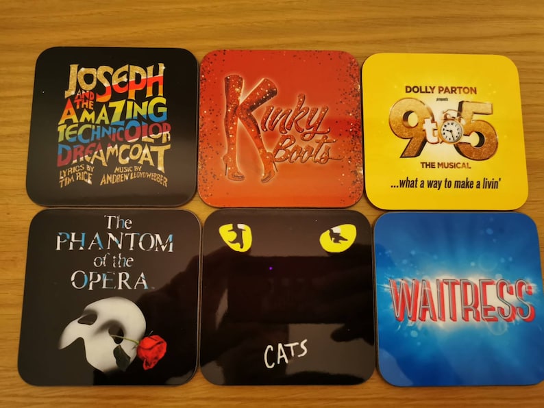 May include: Six square coasters featuring various Broadway show logos. The coasters are black, red, yellow, blue, and white with colorful text and images. The shows featured are Joseph and the Amazing Technicolor Dreamcoat, Kinky Boots, 9 to 5, The Phantom of the Opera, Cats, and Waitress.