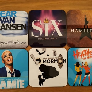 May include: Six coasters featuring Broadway show logos. The coasters are square and have a glossy finish. The logos are printed in various colors and fonts. The coasters feature the following shows: Dear Evan Hansen, Six, Hamilton, The Book of Mormon, and Heathers.