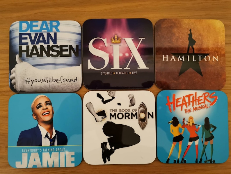 May include: Six coasters featuring Broadway show logos. The coasters are square and have a glossy finish. The logos are printed in various colors and fonts. The coasters feature the following shows: Dear Evan Hansen, Six, Hamilton, The Book of Mormon, and Heathers.