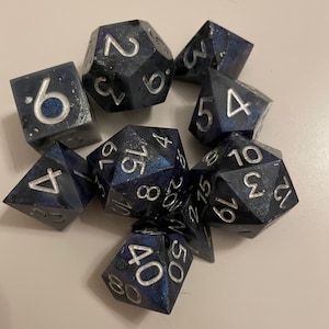 May include: A set of eight black and blue dice with silver numbers. The dice are scattered on a white surface.