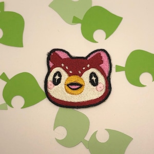 May include: Embroidered patch of a red and white owl with pink cheeks and sparkly eyes. The owl is wearing a white shirt with a yellow beak.