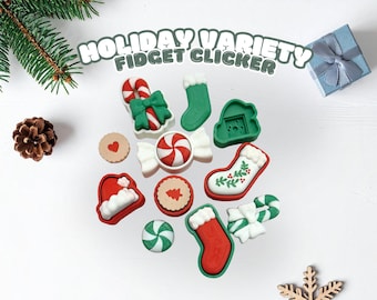 May include: A collection of festive fidget clickers in various shapes, including candy canes, stockings, and cookies, arranged on a white surface. The text "HOLIDAY VARIETY FIDGET CLICKER" is displayed above the items. A pine cone and a small gift box are also present.