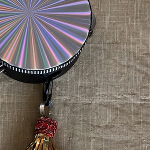 May include: A black tambourine with a rainbow iridescent design and a red, gold, and black tassel.