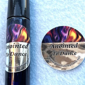 May include: A small glass bottle with a black cap and a colorful label that says "Anointed To Dance" and "www.gloriouscreations.net". The bottle is next to a round sticker with the same design and text.