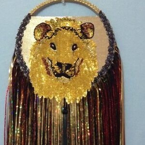 May include: A gold and red beaded dreamcatcher with a lion face made of sequins. The dreamcatcher has a wooden hoop and a black tassel.