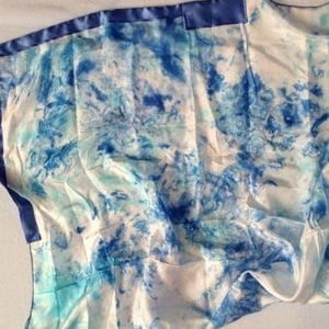 May include: A white silk scarf with a blue and turquoise abstract design. The scarf has a blue satin border.