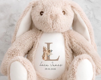 May include: A plush beige rabbit stuffed animal with long ears and white foot pads. The center of the chest features a white patch printed with a large letter L, a small rabbit illustration, the name Luca James, and the date 28.01.2026.
