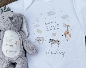 Könnte beinhalten: Ein weißer Baby-Strampler mit dem Text "Born in 2025" und einem Namen. Der Strampler zeigt Illustrationen von Tieren und Luftballons. Ein graues Plüsch-Hasenspielzeug liegt neben dem Strampler, ebenfalls mit dem Namen und Tierillustrationen.