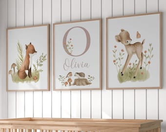 May include: Three framed nursery art prints. The first features a fox in a forest setting. The second has the letter "O" with the name "Olivia". The third print shows a fawn with a butterfly. All prints have a light wood frame.