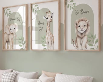 May include: Three framed animal art prints in wooden frames. The prints depict an elephant, giraffe, and lion, set against a soft green arch background with botanical details. The prints feature the phrases "Dream Big", "Stand Tall", and "Be Brave".