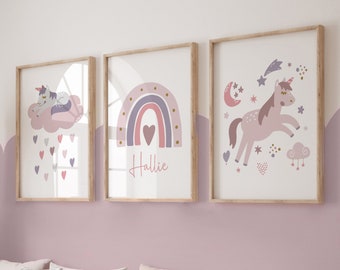 May include: Three framed art prints with a unicorn, rainbow, and stars theme. The prints feature soft pink, purple, and gold colors. One print has the name "Hallie" written in cursive. The prints are displayed above a wooden bench with pillows.