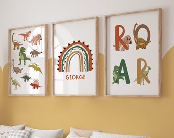 May include: Three framed art prints with a dinosaur theme. One print features various dinosaur illustrations, another has a rainbow with the name "GEORGE", and the third spells "ROAR" with dinosaur images. The frames are light brown.
