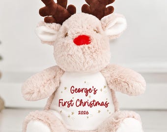 May include: A plush reindeer toy with soft beige fur, dark brown antlers, and a bright red nose. The center of the chest features a white patch with the red text George's First Christmas 2026 surrounded by small gold star accents.