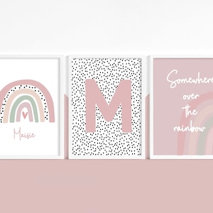 May include: Three framed art prints with a soft pink and white color scheme. The prints feature a rainbow, the letter "M" on a dotted background, and the phrase "Somewhere over the rainbow."