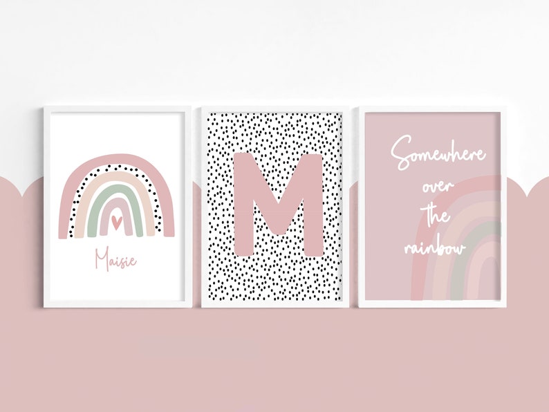 May include: Three framed art prints with a soft pink and white color scheme. The prints feature a rainbow, the letter "M" on a dotted background, and the phrase "Somewhere over the rainbow."