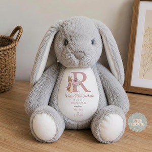 May include: A soft, grey plush rabbit with long ears and white foot pads. The rabbit features a white oval patch on its chest printed with a large letter R, a small rabbit illustration, and the text: Rosie Mae Jackson, born on 10/06/2026, weighing 9lb 4oz at 2.03am.