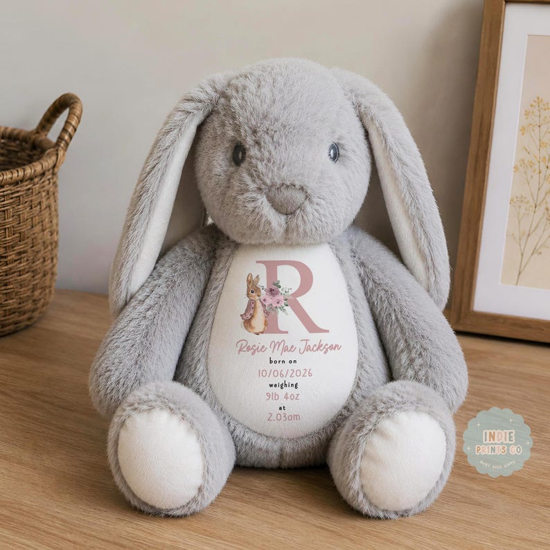 May include: A soft, grey plush rabbit with long ears and white foot pads. The rabbit features a white oval patch on its chest printed with a large letter R, a small rabbit illustration, and the text: Rosie Mae Jackson, born on 10/06/2026, weighing 9lb 4oz at 2.03am.