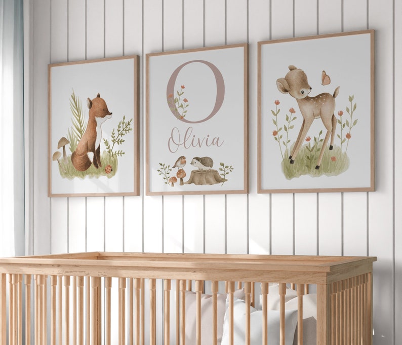 May include: Three framed nursery art prints. The first features a fox in a forest setting. The second has the letter "O" with the name "Olivia". The third print shows a fawn with a butterfly. All prints have a light wood frame.
